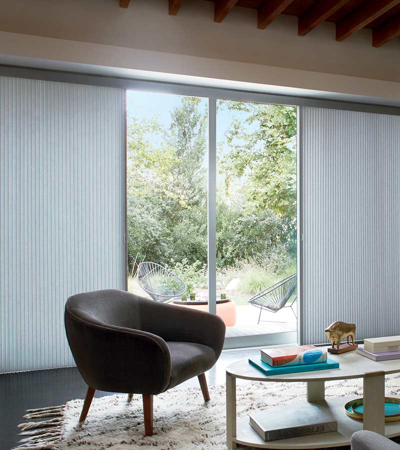 blue vertiglide shades that are half open in living room with large gray chair