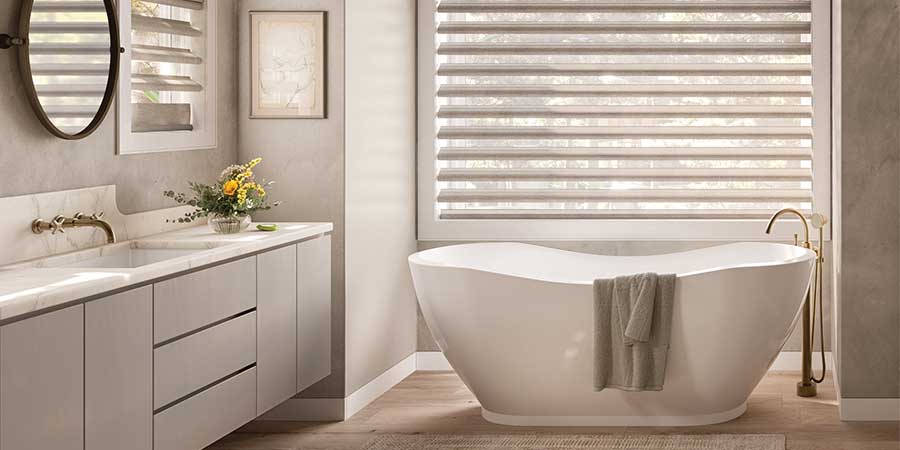 neutral tone bathroom with white tub and floor to ceiling windows shades